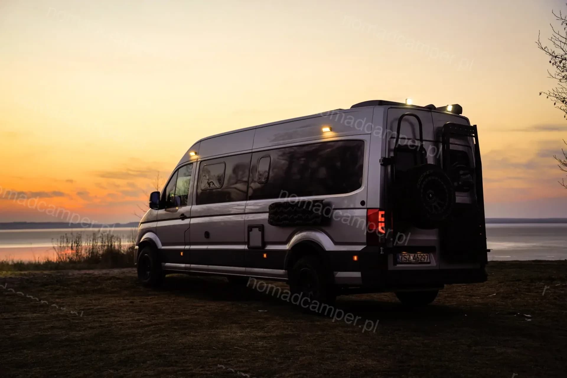 Nomad Camper MAN TGE o zachodzie słońca nad wodą, włączone światła dachowe